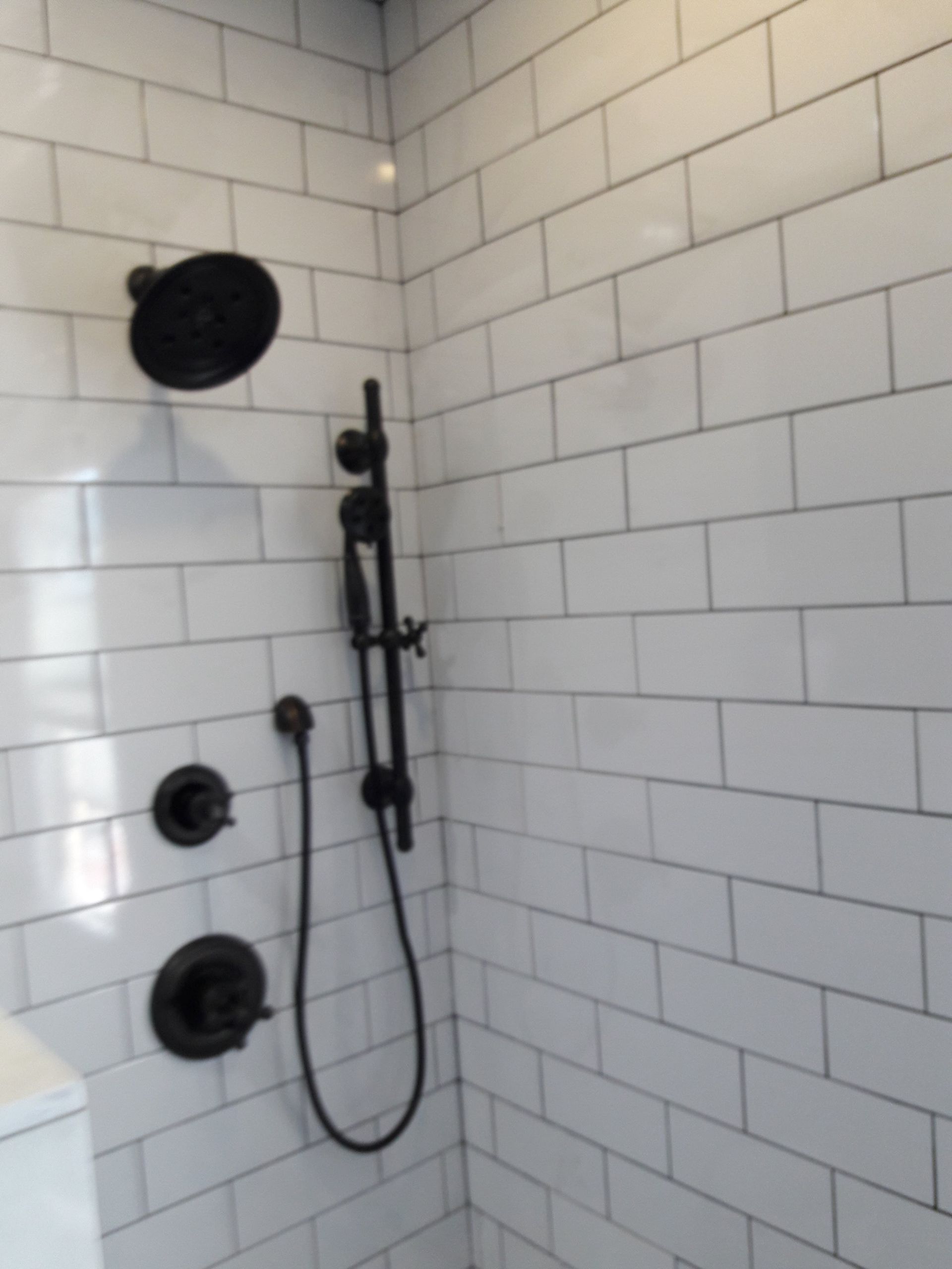 A shower stall with white subway tile walls and a matte black shower head, handheld sprayer, and control valves.