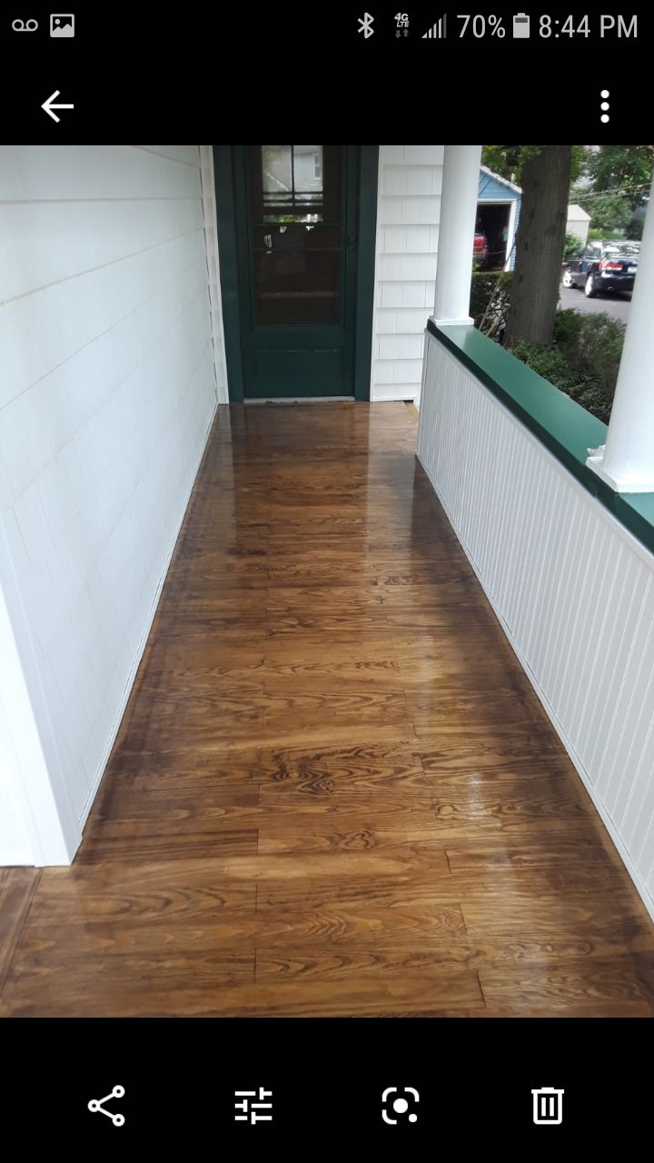 A view down a residential front porch with shiny, stained wood flooring, white siding, and a dark green entry door.