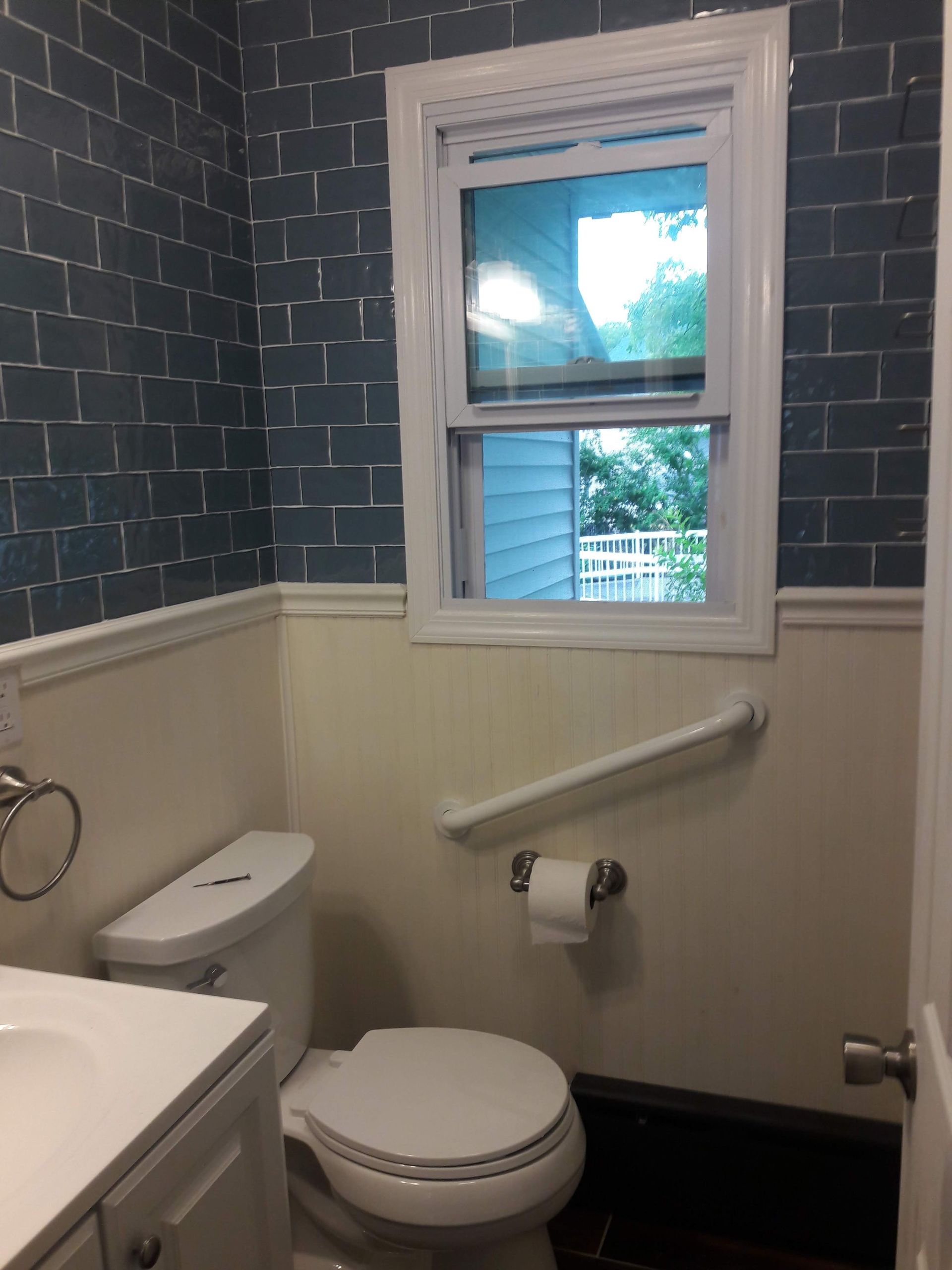 A small, accessible bathroom with blue brick-patterned wallpaper, white wainscoting, a toilet, and a white grab bar.