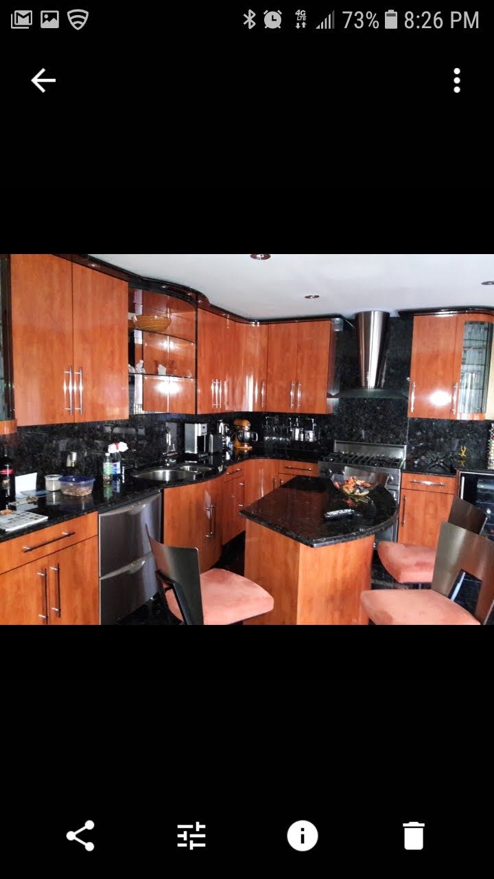 A kitchen with warm-toned wood cabinets, black countertops, stainless steel appliances, and a central island with chairs.