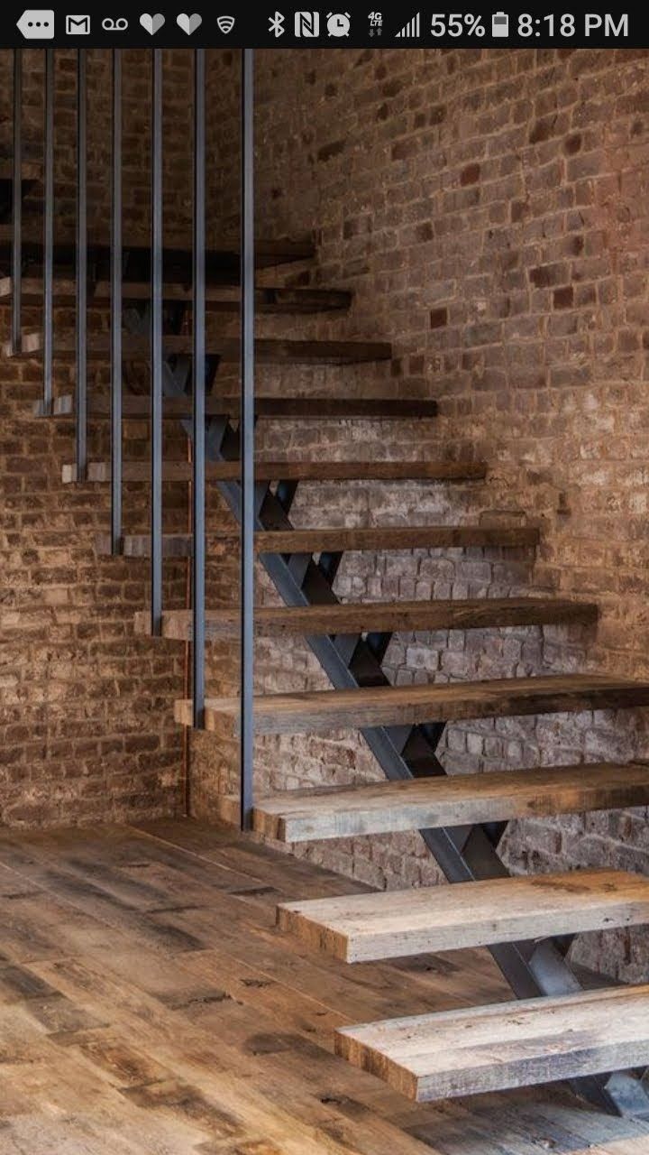 Floating staircase with rustic wooden treads and thin metal balusters against a textured brick wall.