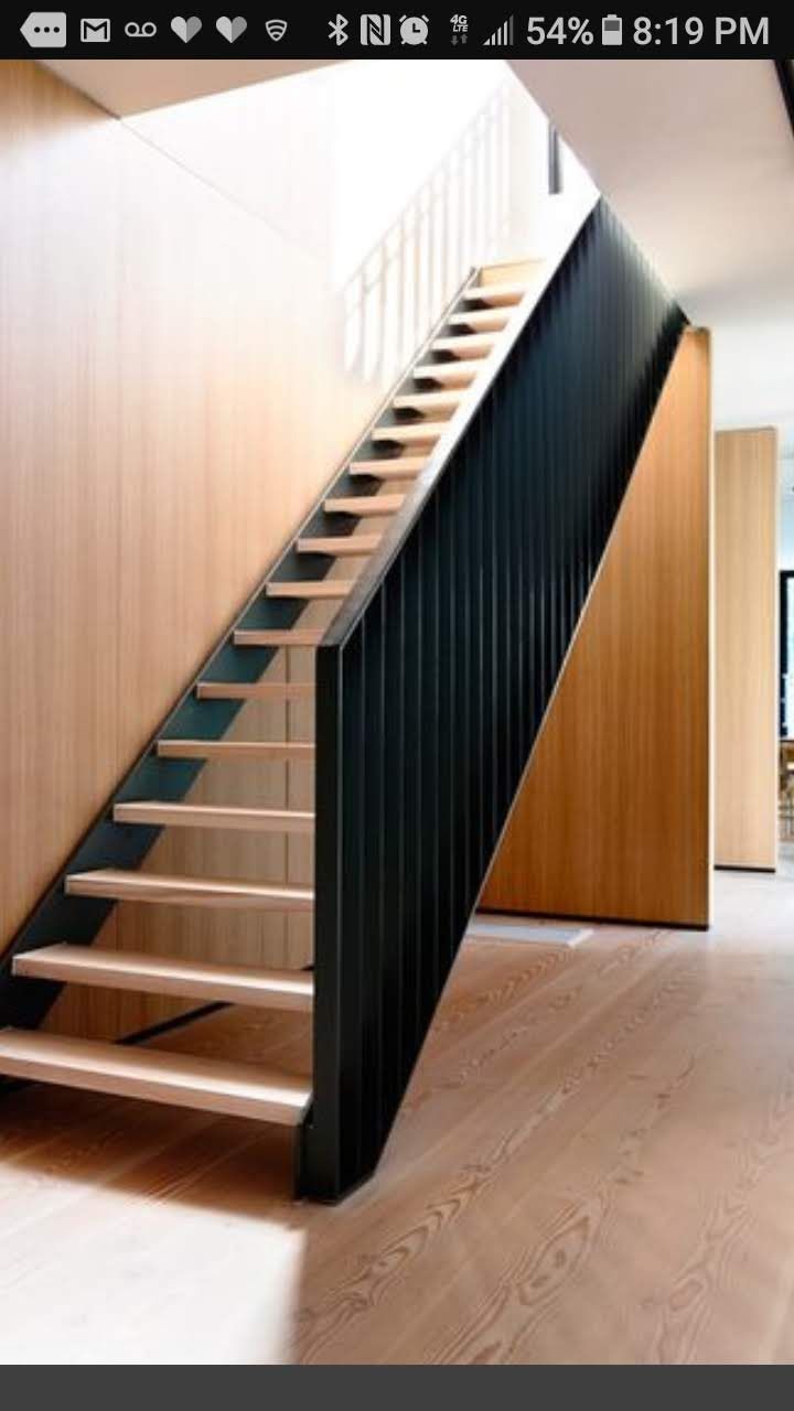 A staircase with light wood treads and a black metal railing inside a modern home with wood-paneled walls.