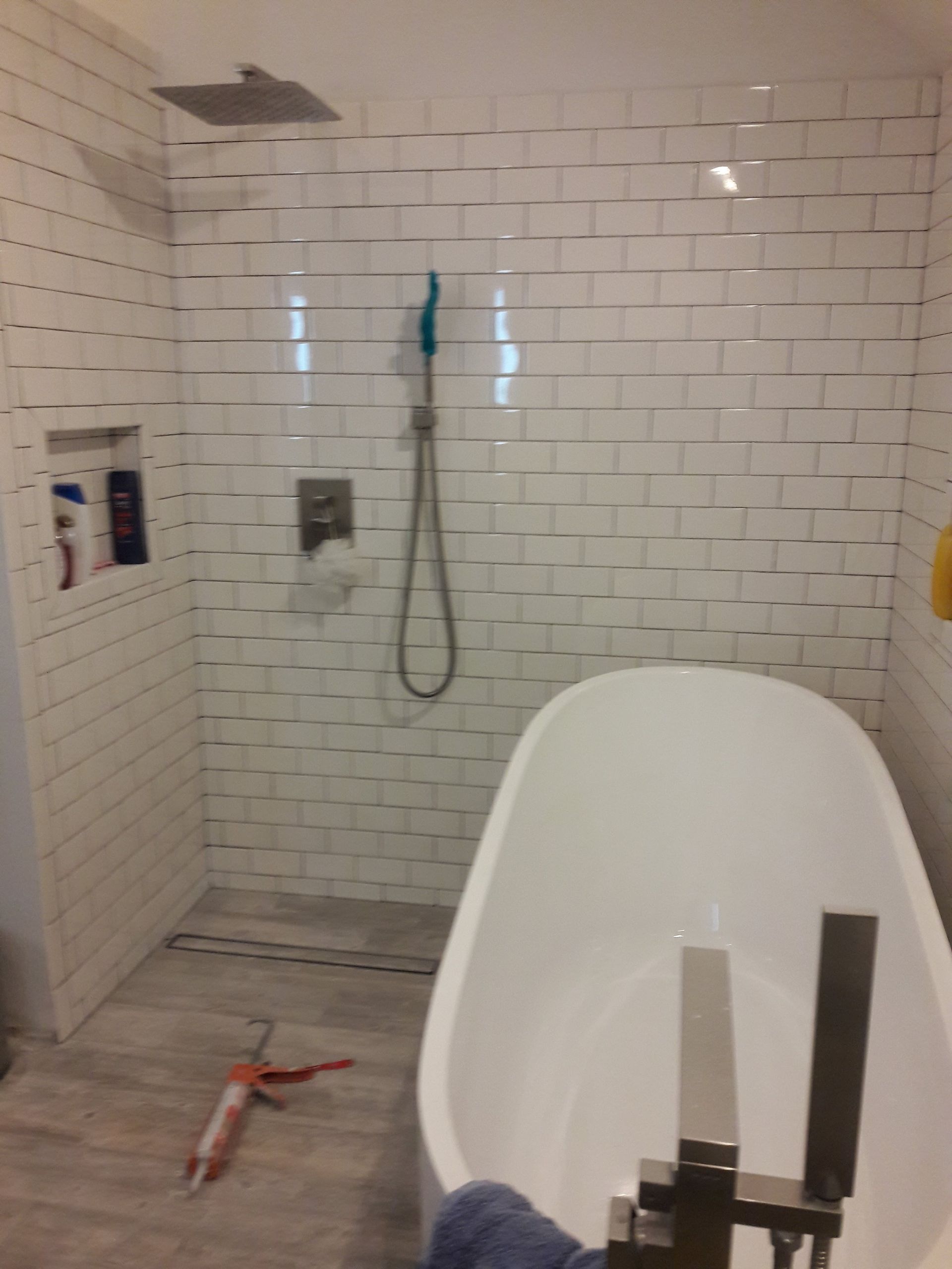 A modern bathroom featuring a white freestanding bathtub, tiled walls, a rain showerhead, and a handheld faucet.