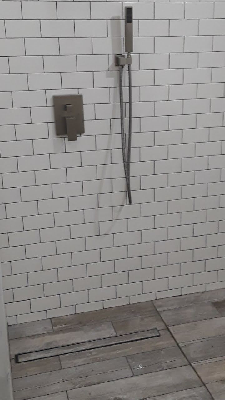 A walk-in shower with white subway tiles, a brushed nickel handheld showerhead, a wall-mount faucet, and a floor drain.