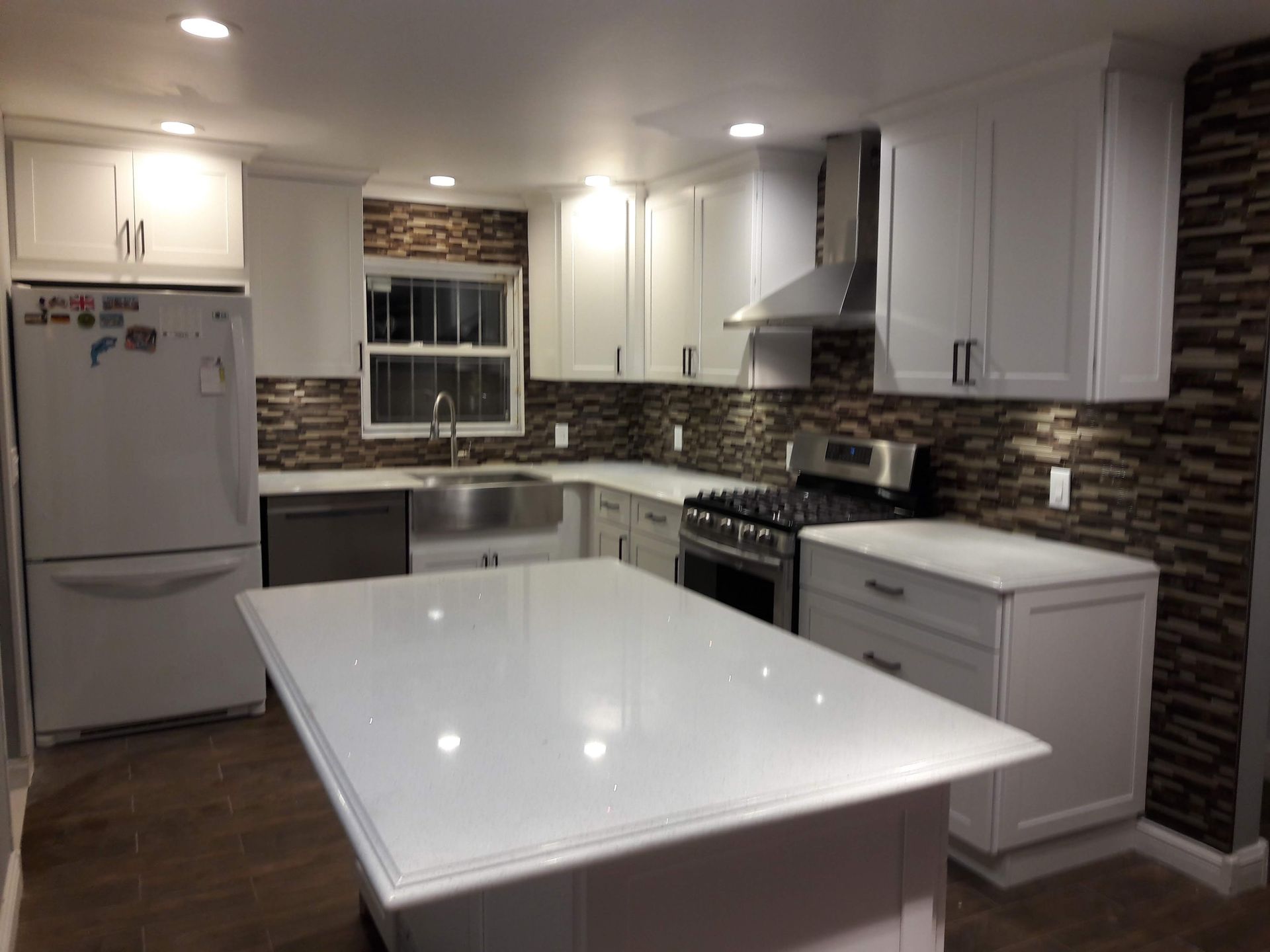 A modern kitchen with white cabinets, a large central island, stainless steel appliances, and a dark stone backsplash.