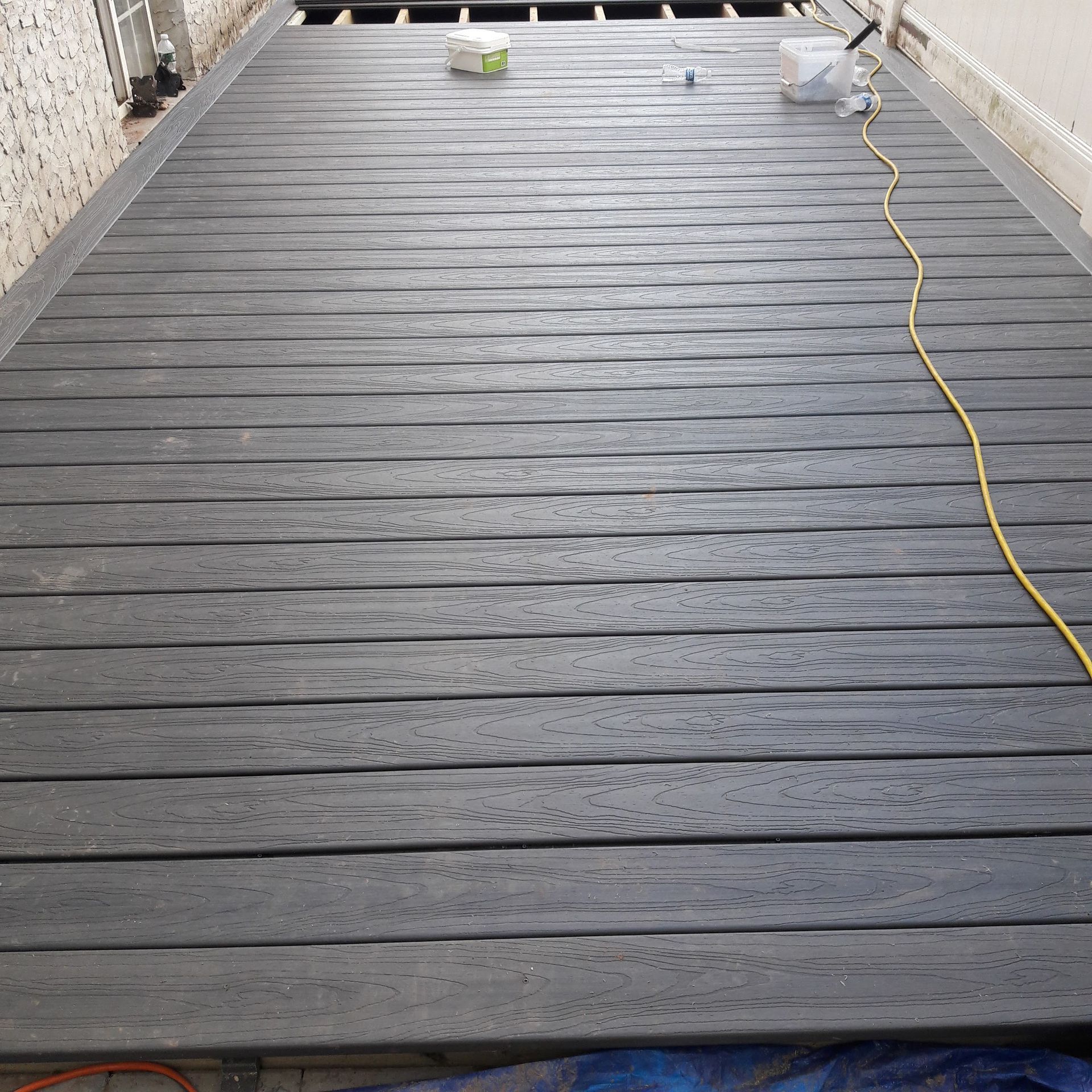A partially finished gray composite deck with a yellow extension cord lying across the surface.