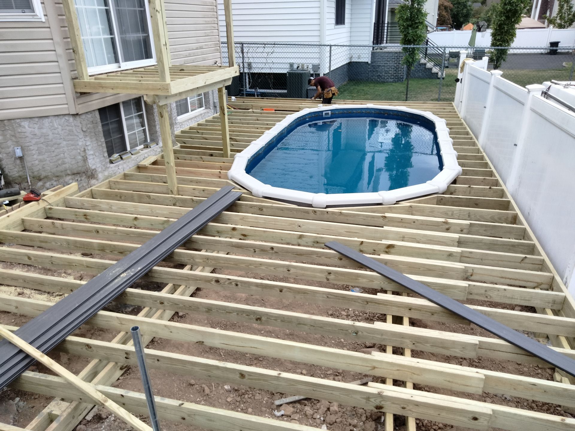 An unfinished wooden deck frame surrounding an oval above-ground swimming pool in a residential backyard.