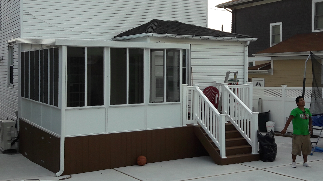 A white sunroom addition with brown base panels, a white staircase, and a person standing on a patio beside it.