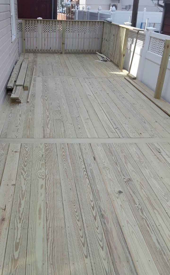 A newly constructed wooden deck featuring light-colored planks, a lattice-style railing, and stacked lumber at the side.