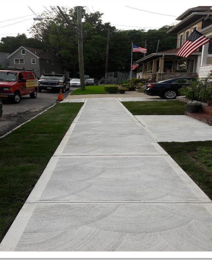 A newly poured concrete walkway with decorative circular patterns leading to steps in front of a residential house.