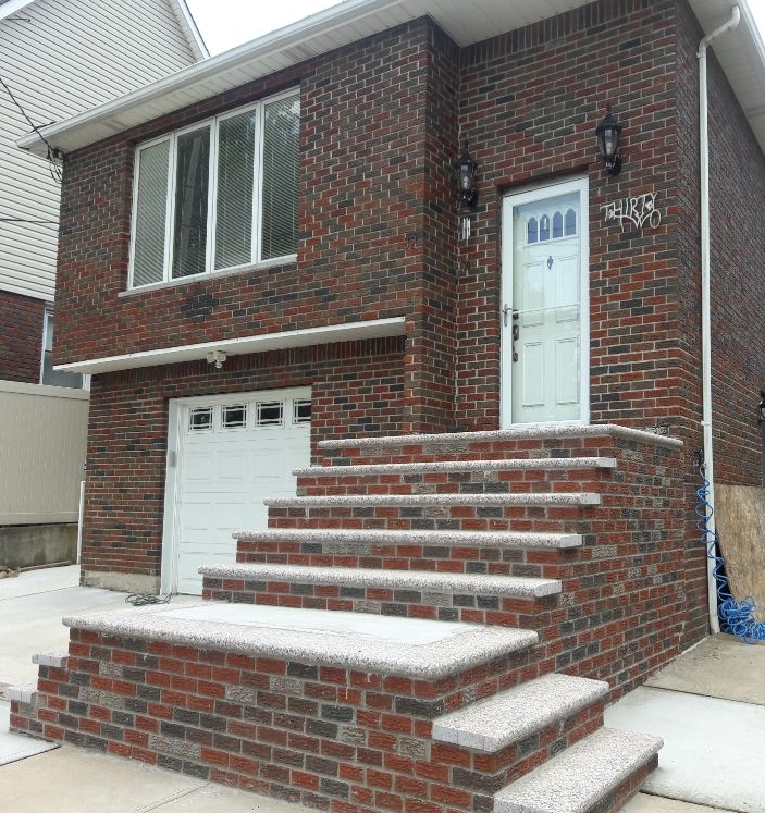 A brick house exterior featuring a front entrance with new stone steps and a white garage door.
