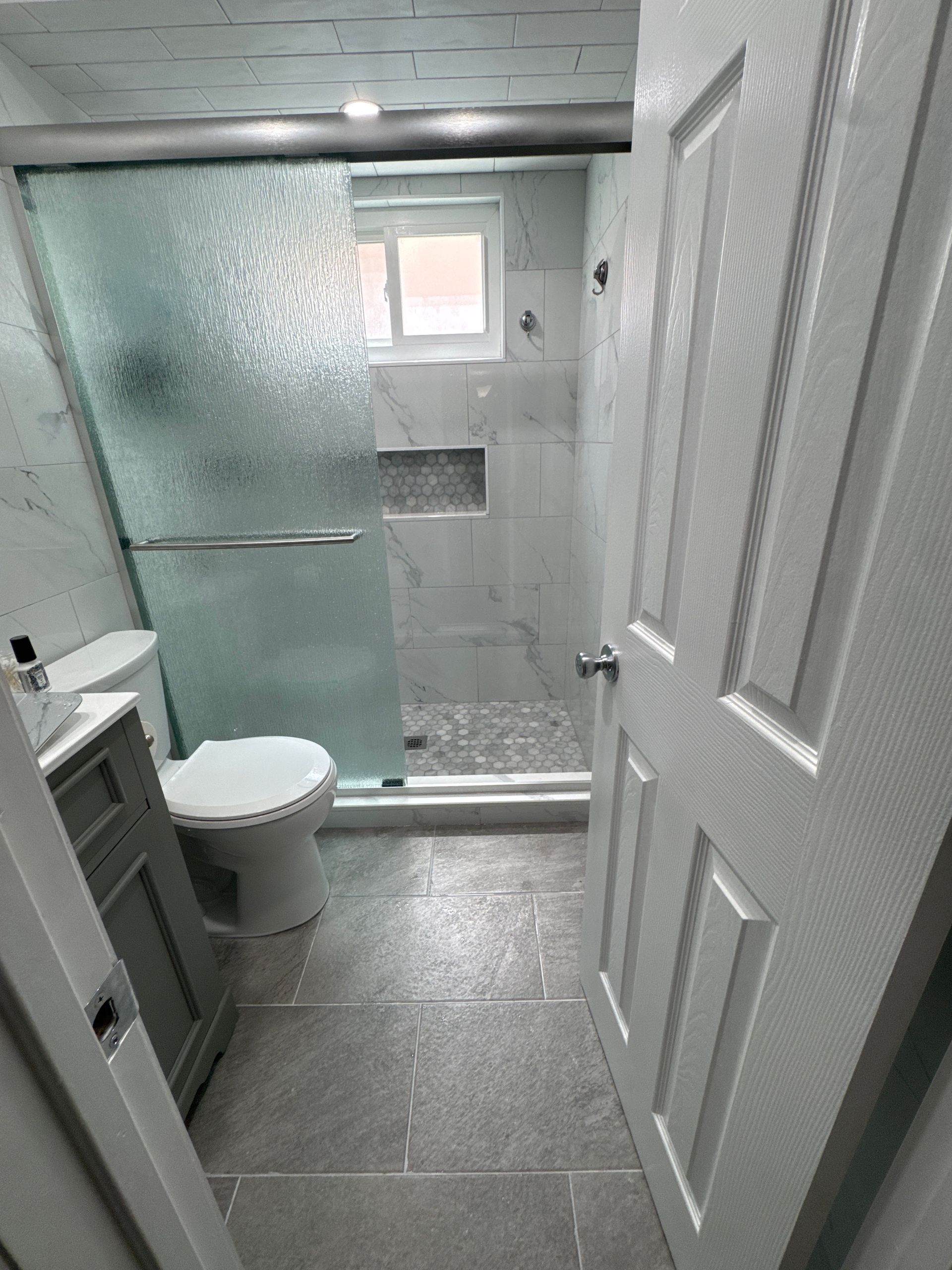Small tiled bathroom with shower stall, toilet, frosted glass door, and white paneled door.