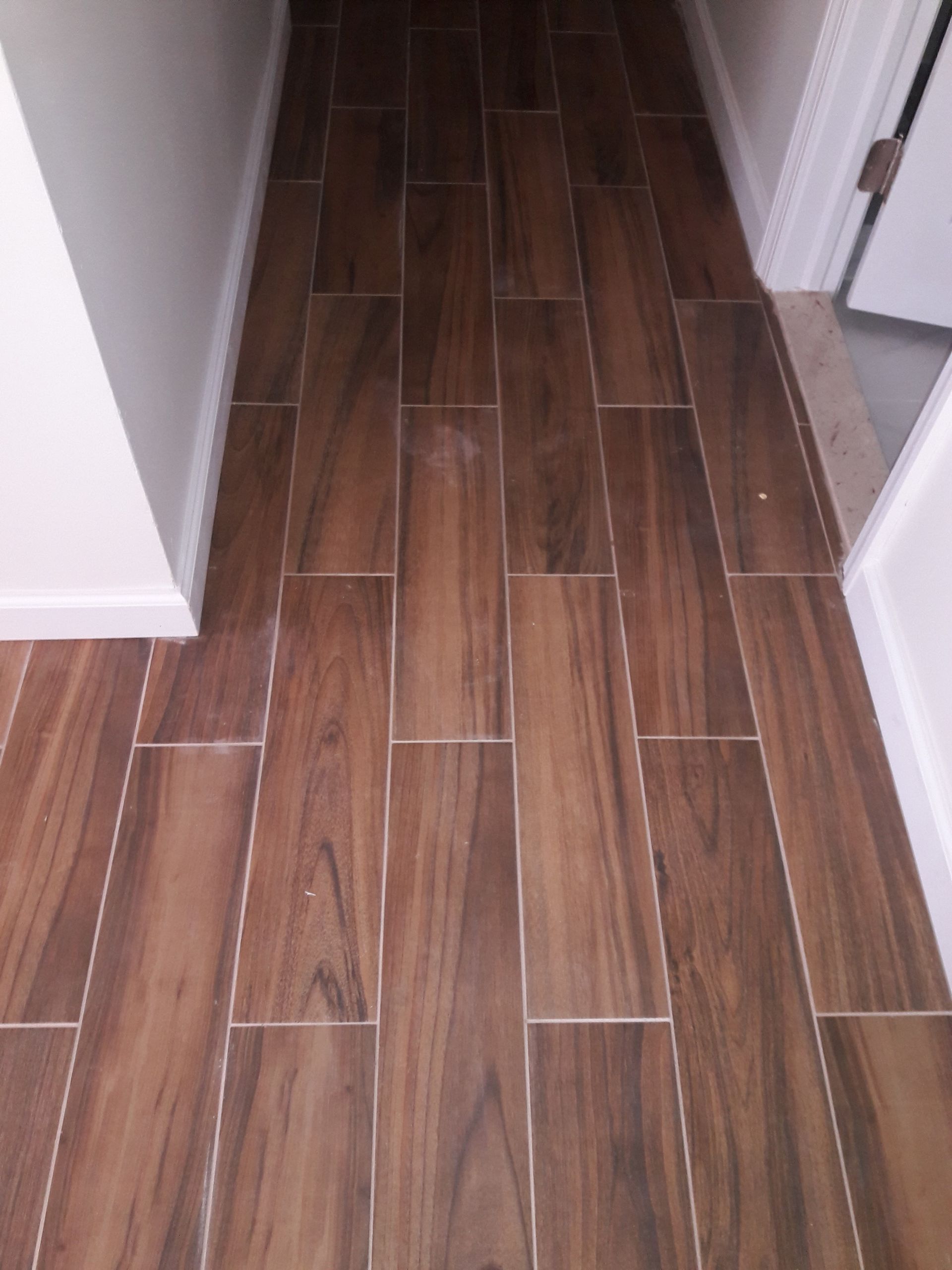 A hallway floor covered in dark, wood-look rectangular tiles laid in a staggered pattern between white walls.