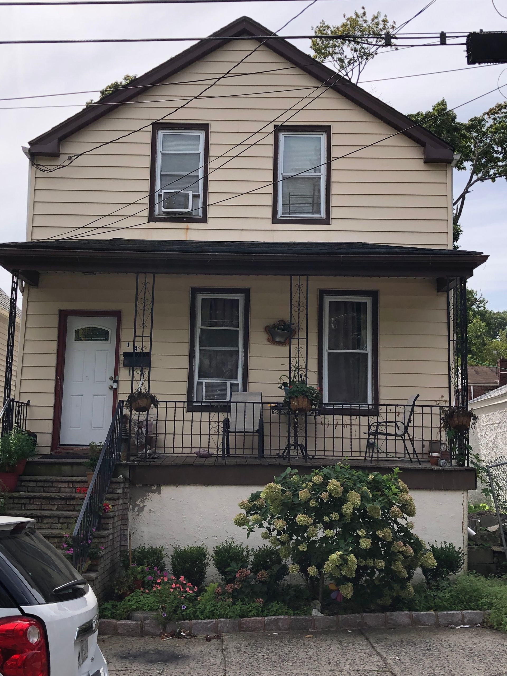 A two-story, light-yellow house with a front porch, steps, and a bush in the yard.