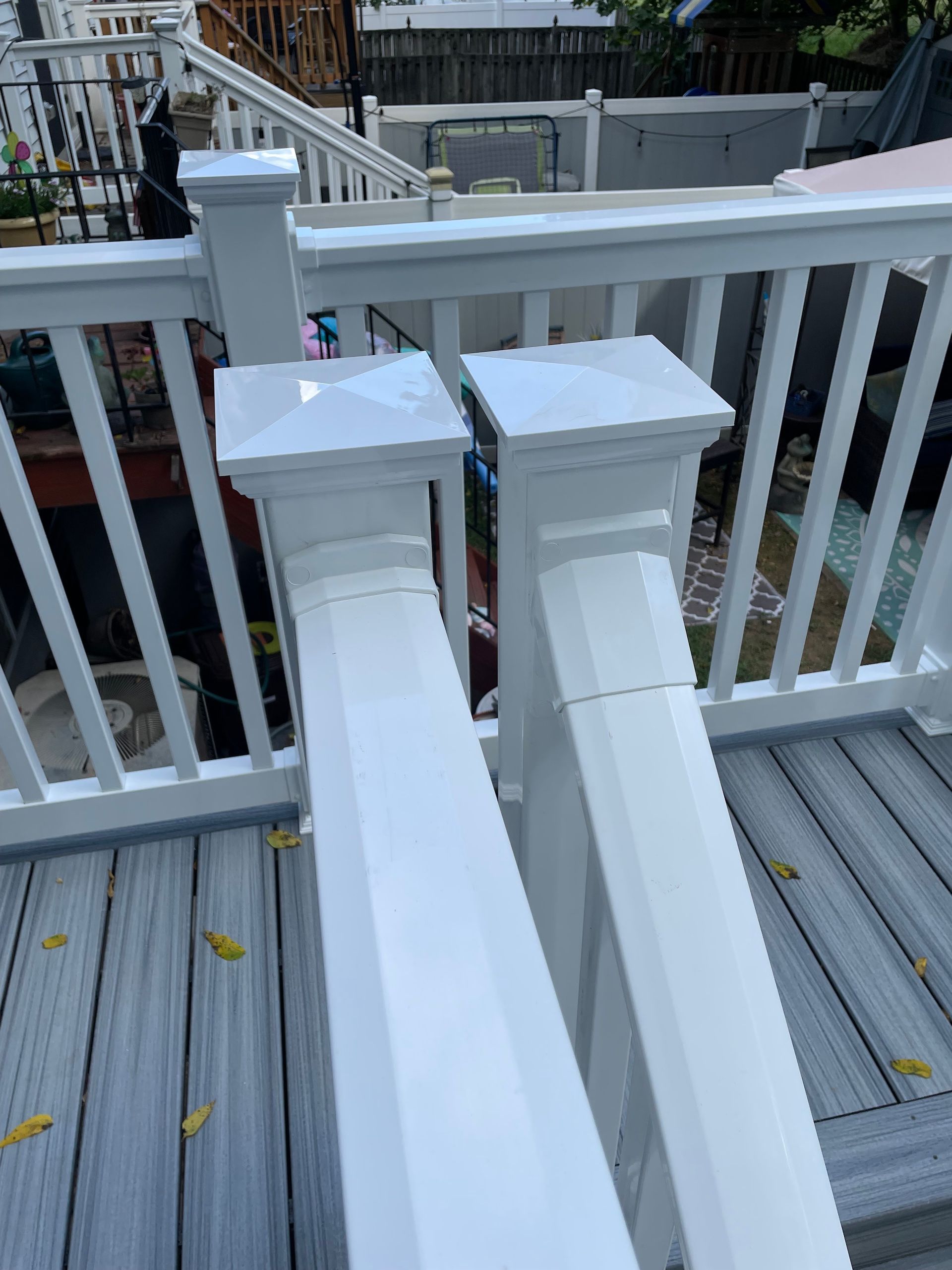 Two white vinyl deck post caps and railings installed on a grey composite deck.