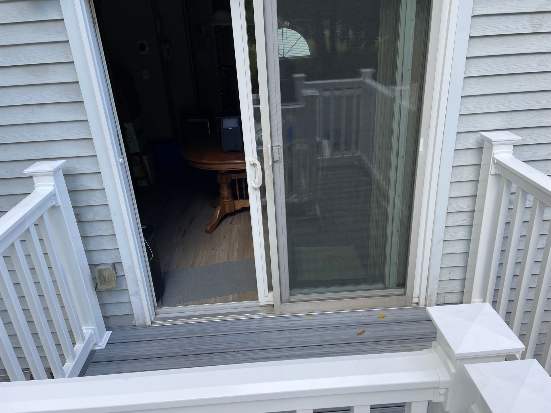 A view from a deck looking through an open sliding glass door into a home with a wooden dining table visible inside.