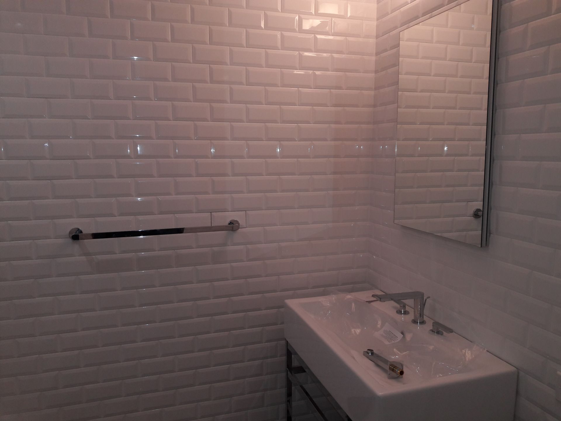 A bathroom vanity with a white sink and chrome faucet against a white subway tile wall with a rectangular mirror.