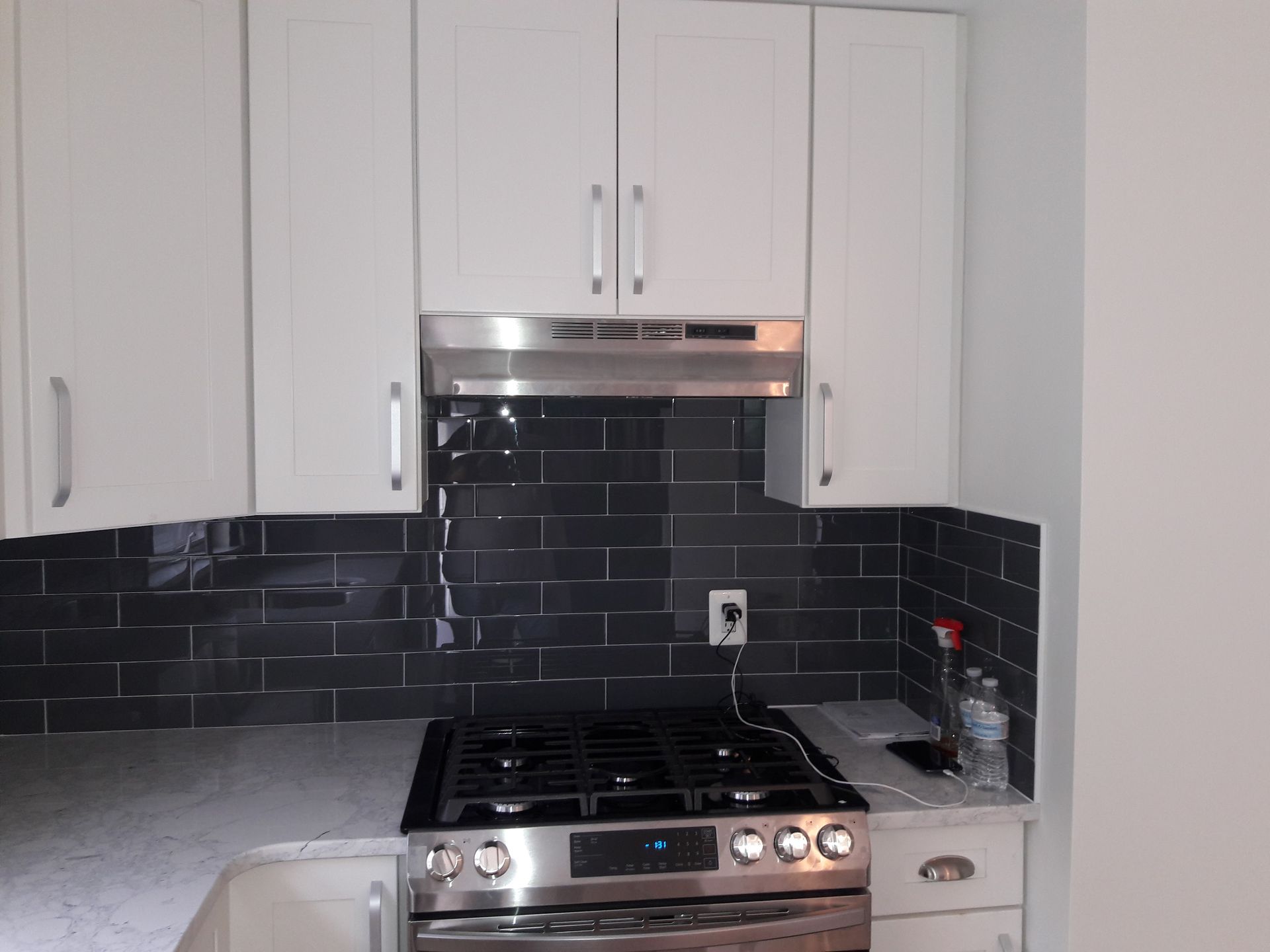 A modern kitchen with white cabinets, dark gray subway tile backsplash, and a stainless steel gas stove.