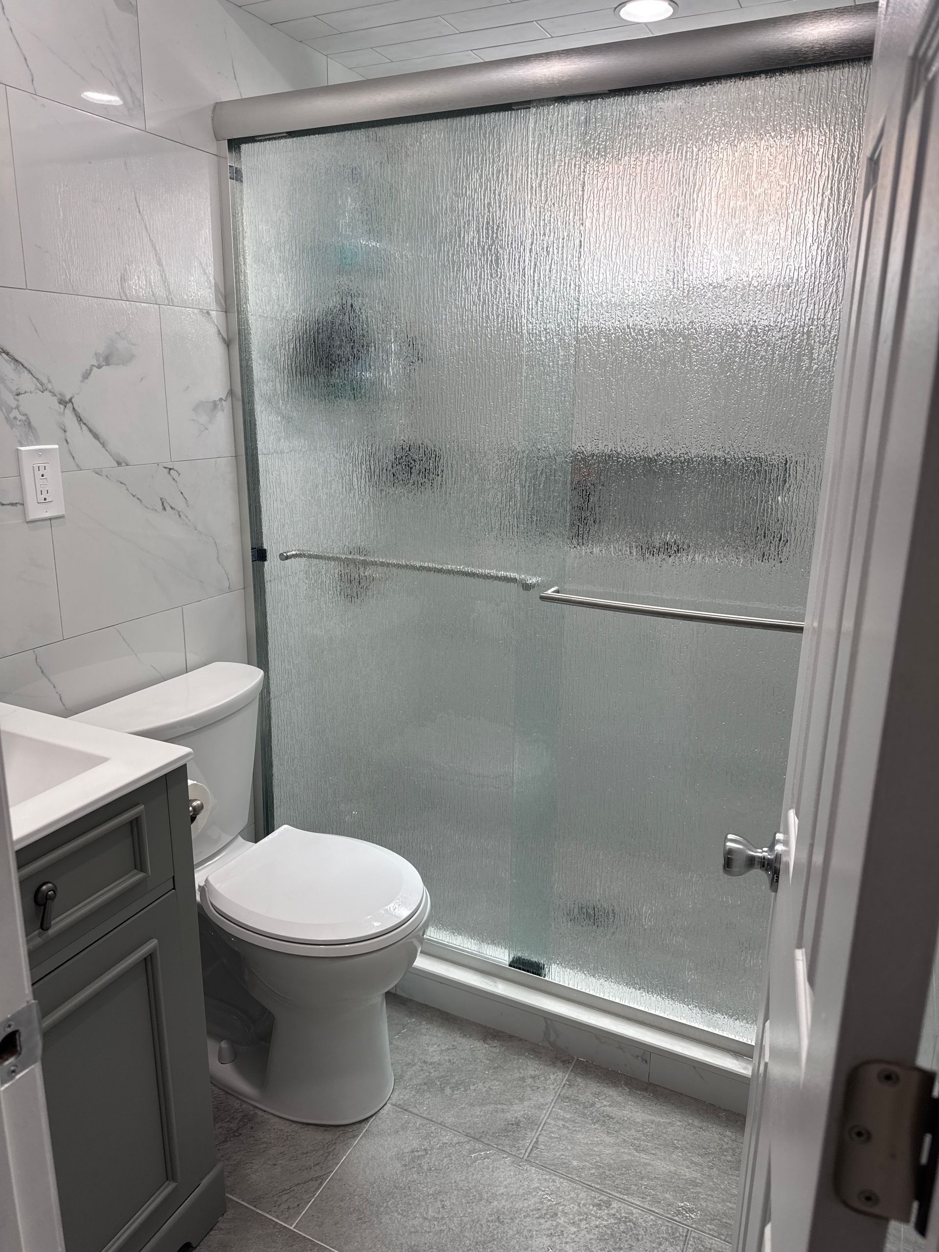 Small bathroom with toilet, sink vanity, and frosted glass shower door.