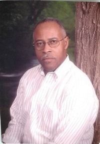 Man in a white striped shirt posing beside a tree outdoors.