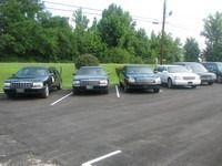 Five parked cars in a lot beside a grassy tree-lined area