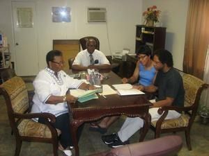 Four people meeting around a wooden table in a small office or living room, reviewing documents.