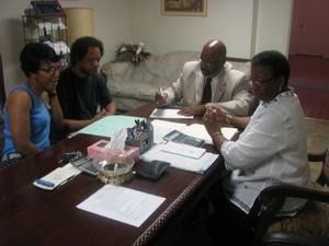 Four people sit around a table in a meeting, discussing documents in a small office.