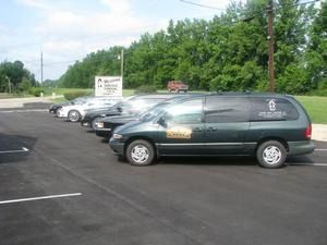 Parking lot with several parked vans and cars near a roadside sign and trees.