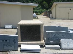 Cemetery gravestones and a granite marker under a pavilion, with white flower holders in front.