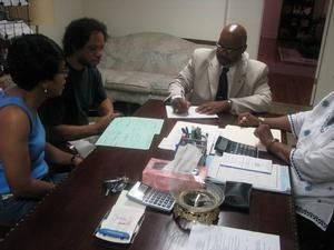 Three people in an office meeting around a table with documents and notebooks.
