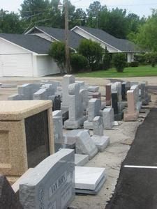 Rows of gray stone memorial headstones displayed on a sidewalk in a suburban neighborhood