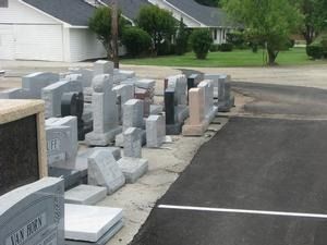 Outdoor display of granite grave markers and monuments lined up beside a paved parking lot