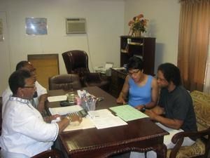 Three people sit around a table in an office, reviewing papers and talking.