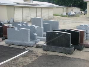 Rows of upright granite grave markers displayed outdoors beside a building.