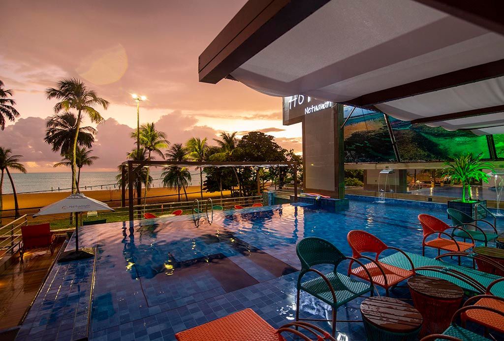 Uma grande piscina com cadeiras e guarda-sóis ao lado da praia Netuanah Praia Hotel
