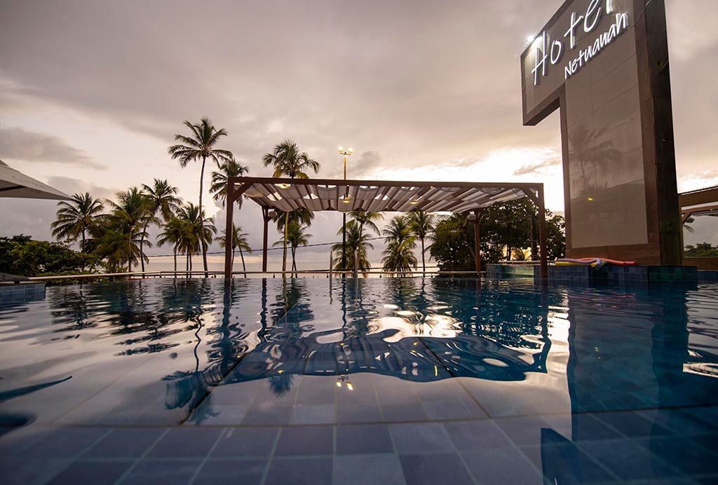 Uma grande piscina com palmeiras ao fundo Netuanah Praia Hotel