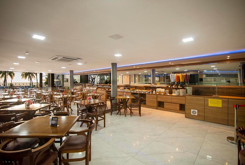 Há muitas mesas e cadeiras no restaurante. Netuanah Praia Hotel
