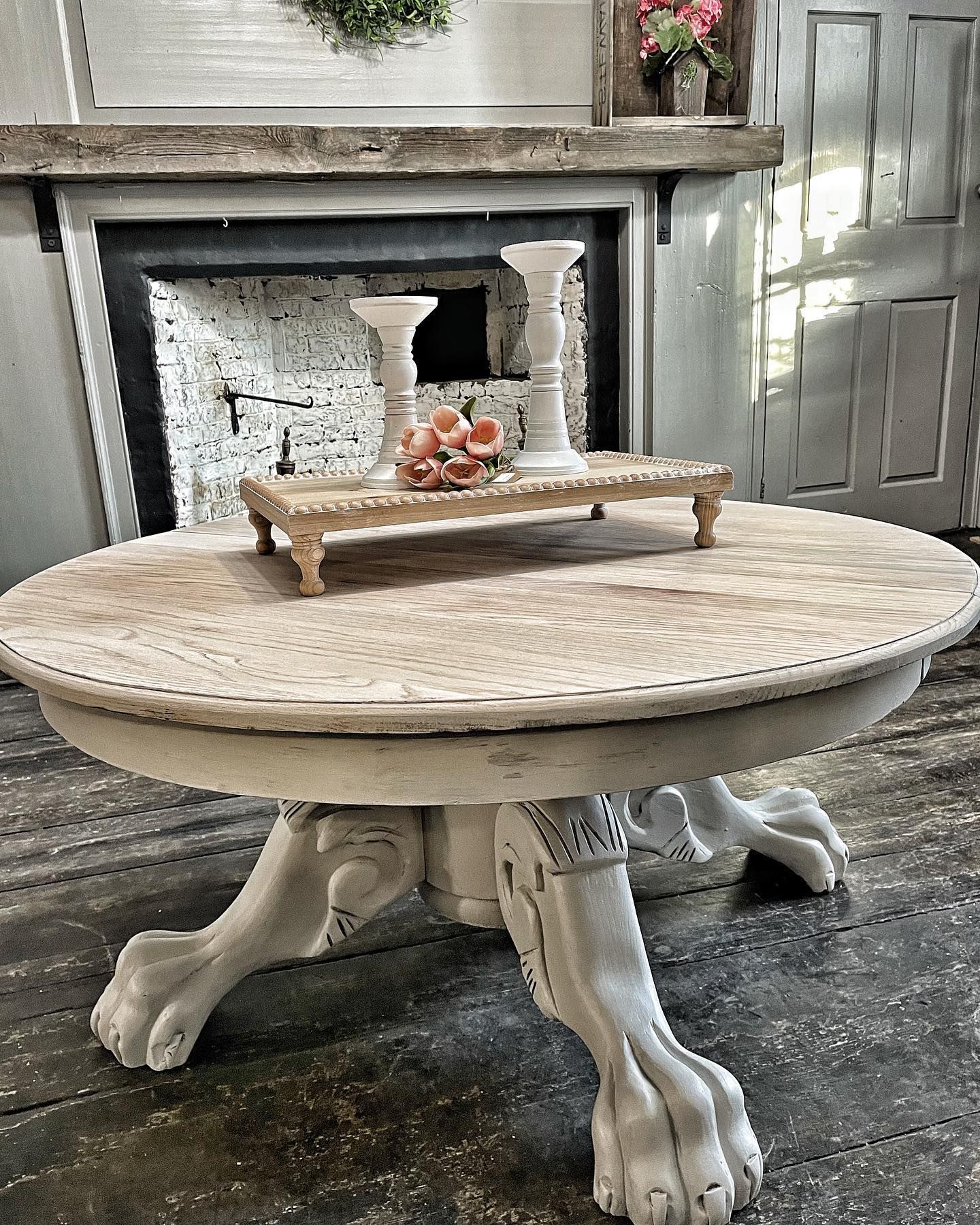 A round table with paw feet is sitting in front of a fireplace.