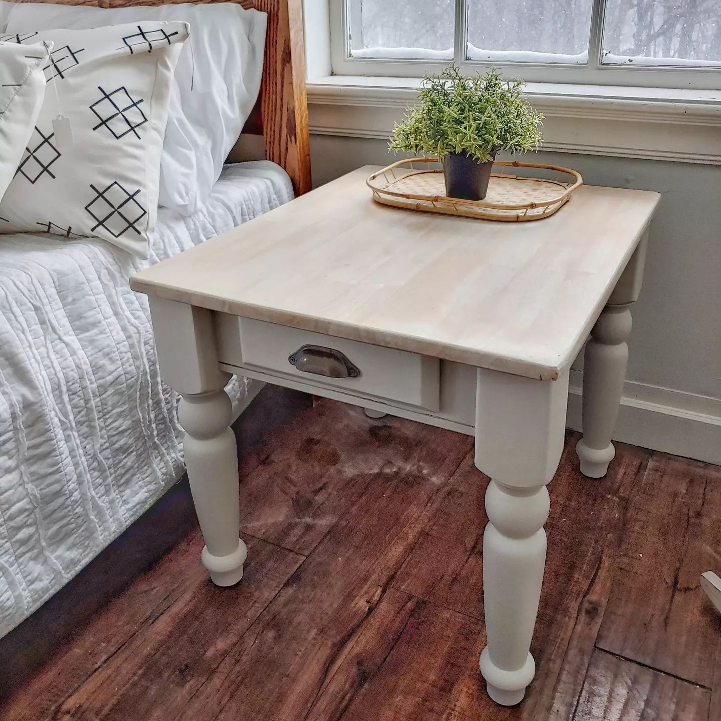A small table with a plant on top of it in a bedroom next to a bed.