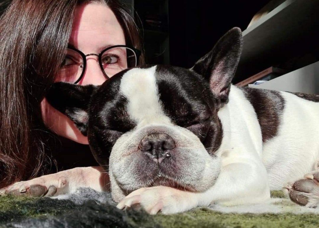 Frau mit Brille und ein schlafender schwarz-weißer französischer Bulldogge, beide in Sonnenlicht getaucht.