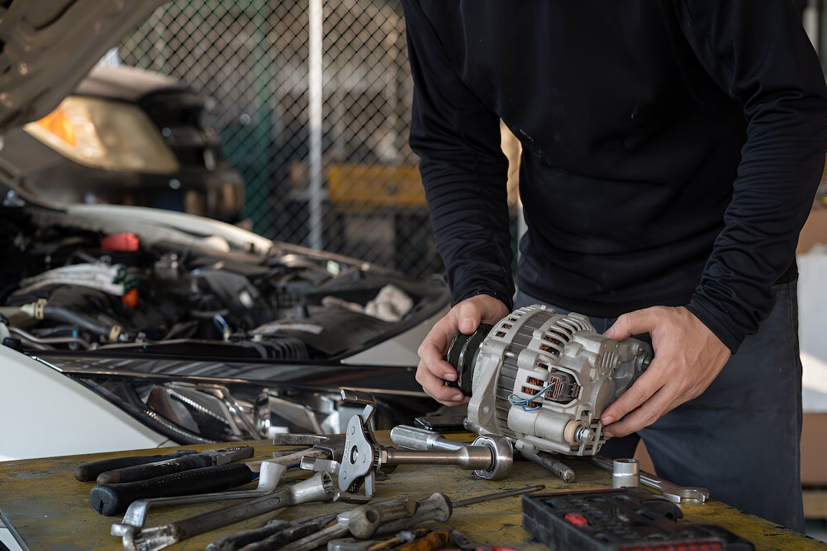 A Man Is Holding A Car Alternator In His Hands While Working On A Car — Cameron Brothers Automotive In Currajong, QLD