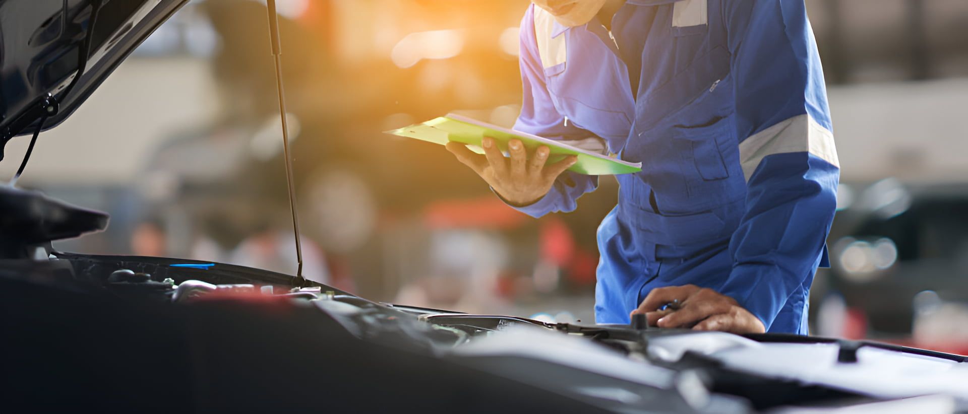 A Mechanic Is Looking At A Clipboard While Working On A Car — Cameron Brothers Automotive In Currajong, QLD