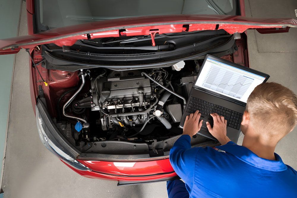 A Man Is Working On The Engine Of A Car With A Laptop — Cameron Brothers Automotive In Currajong, QLD