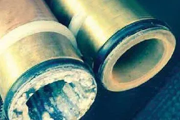 Two brass pipes, one clogged with white mineral buildup. Dark rings around pipe openings.