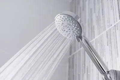 Shower head with water spraying against a tiled wall.