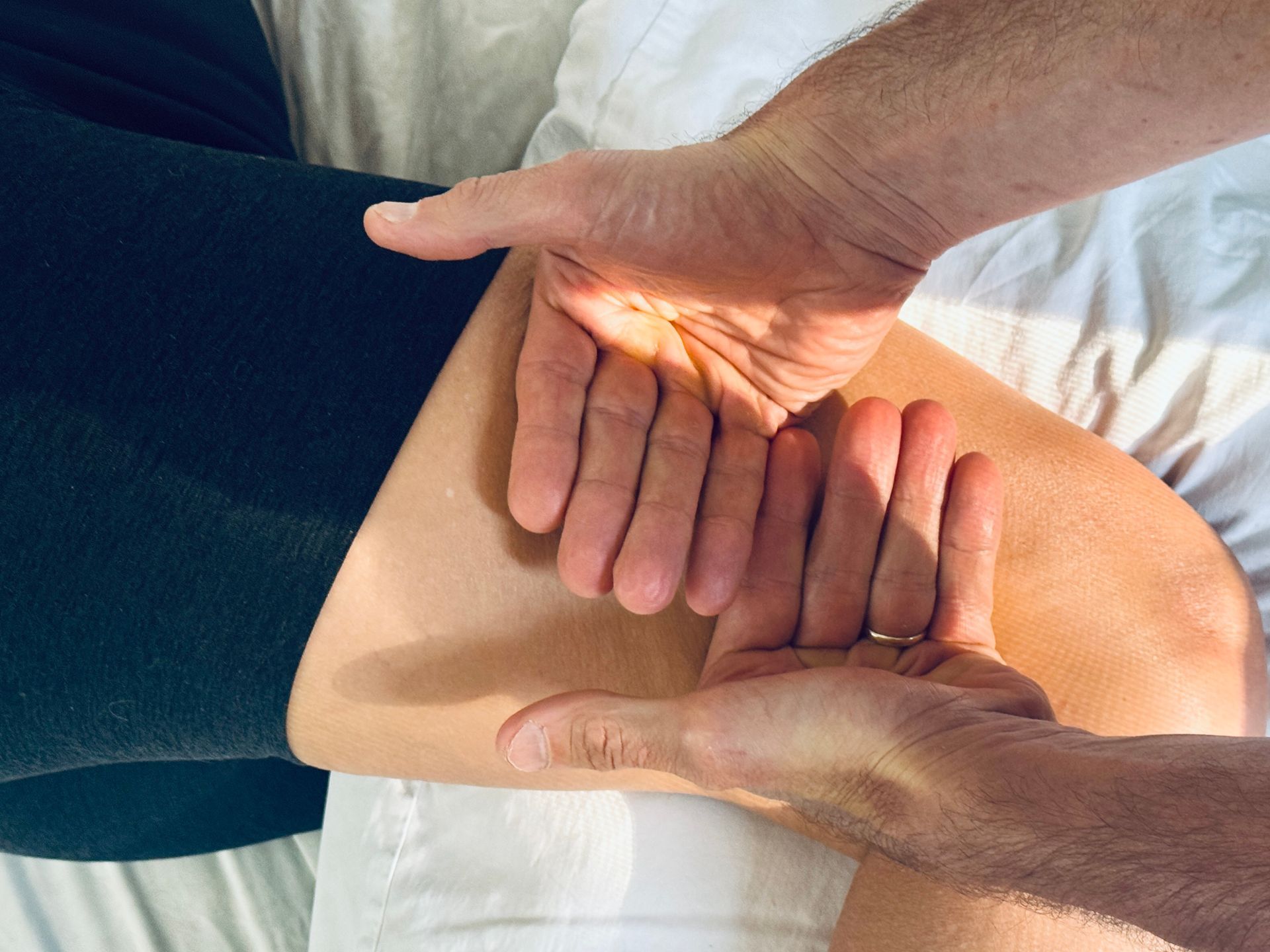 Hands massaging a person's thigh while lying on a white surface. Close up view.
