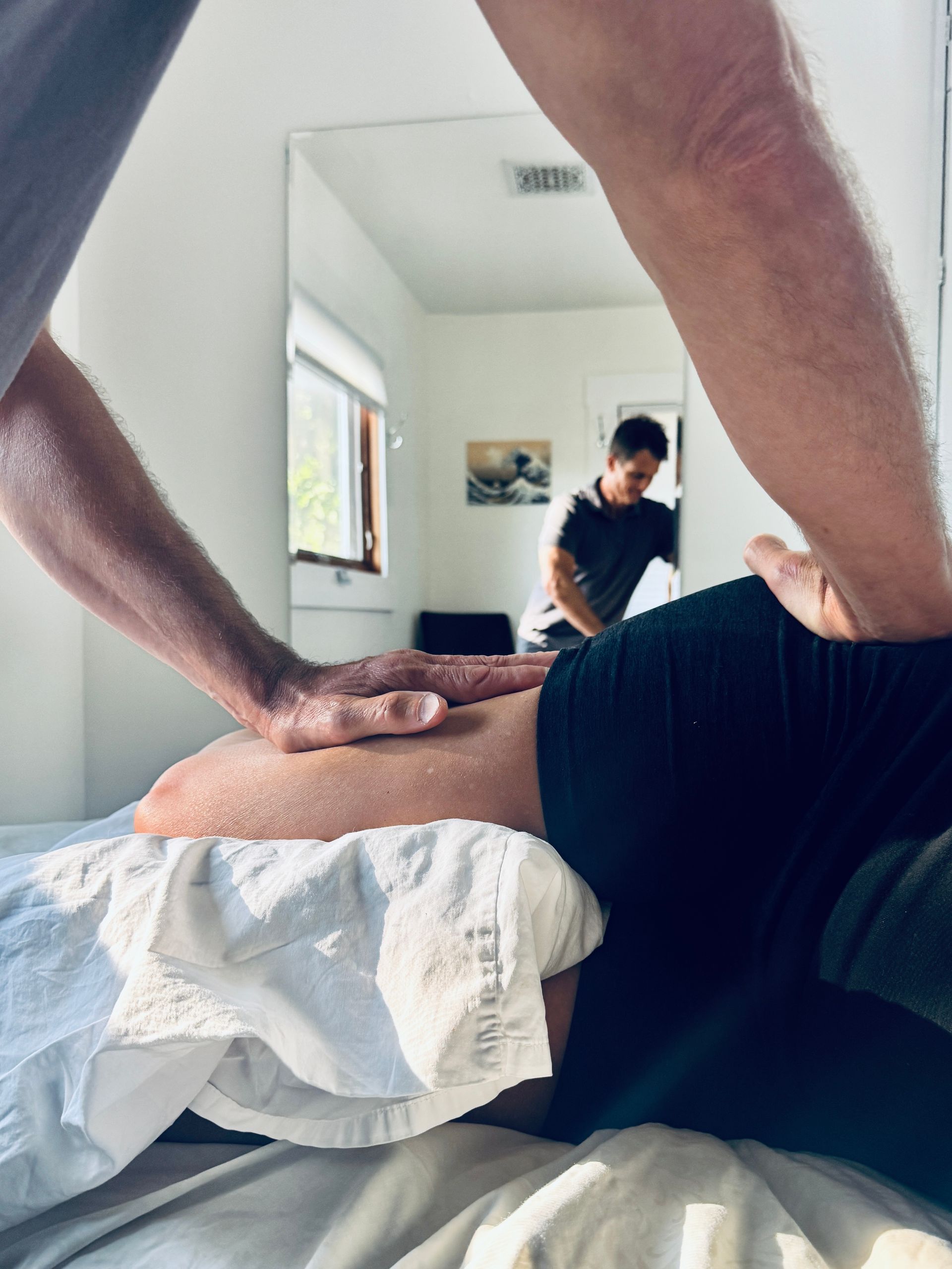 Person receiving massage on back. Therapist's hands on lower back, reflected in a mirror.