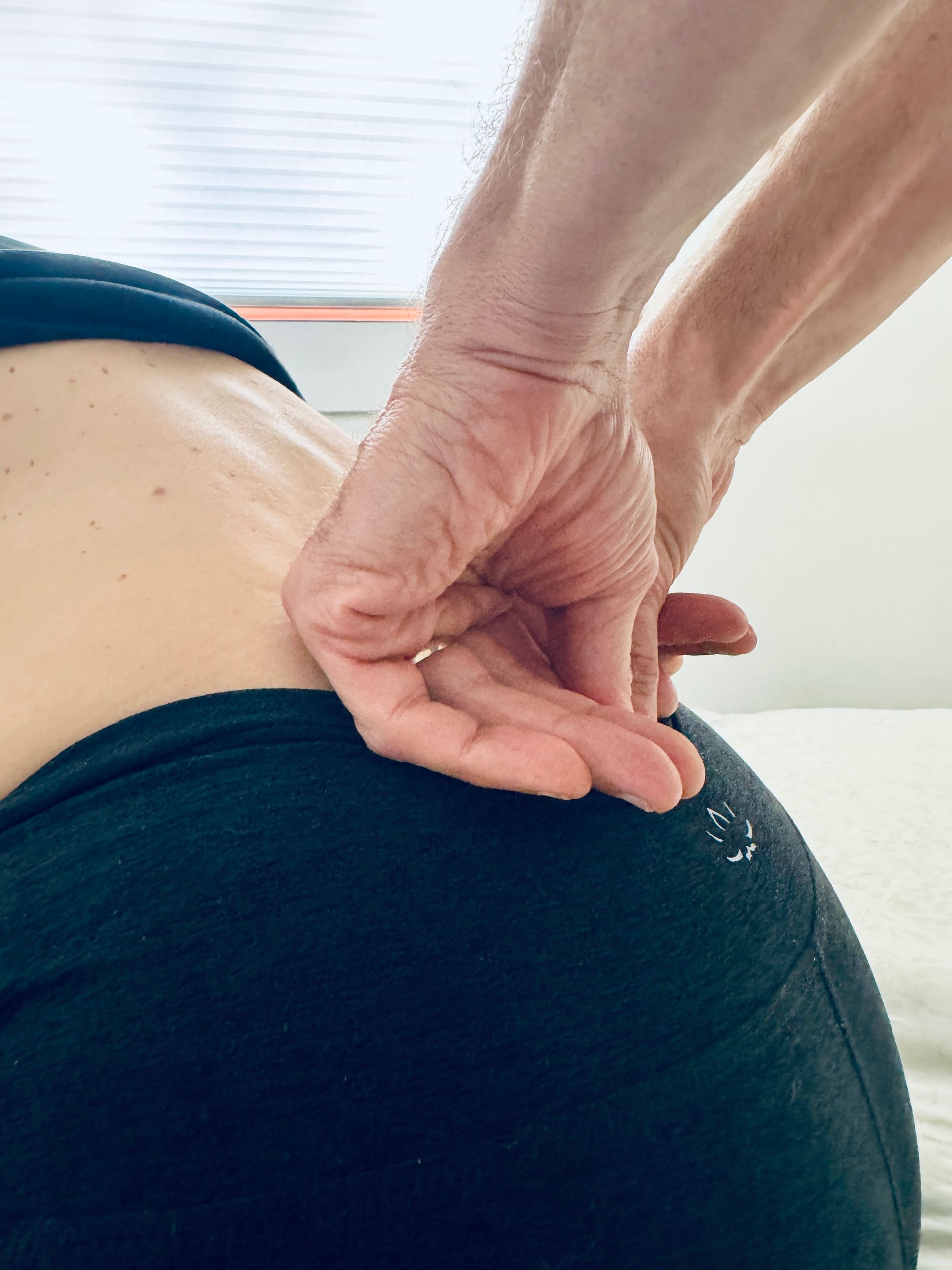Hands on a person's lower back and buttock, likely for massage or physical therapy, indoors.