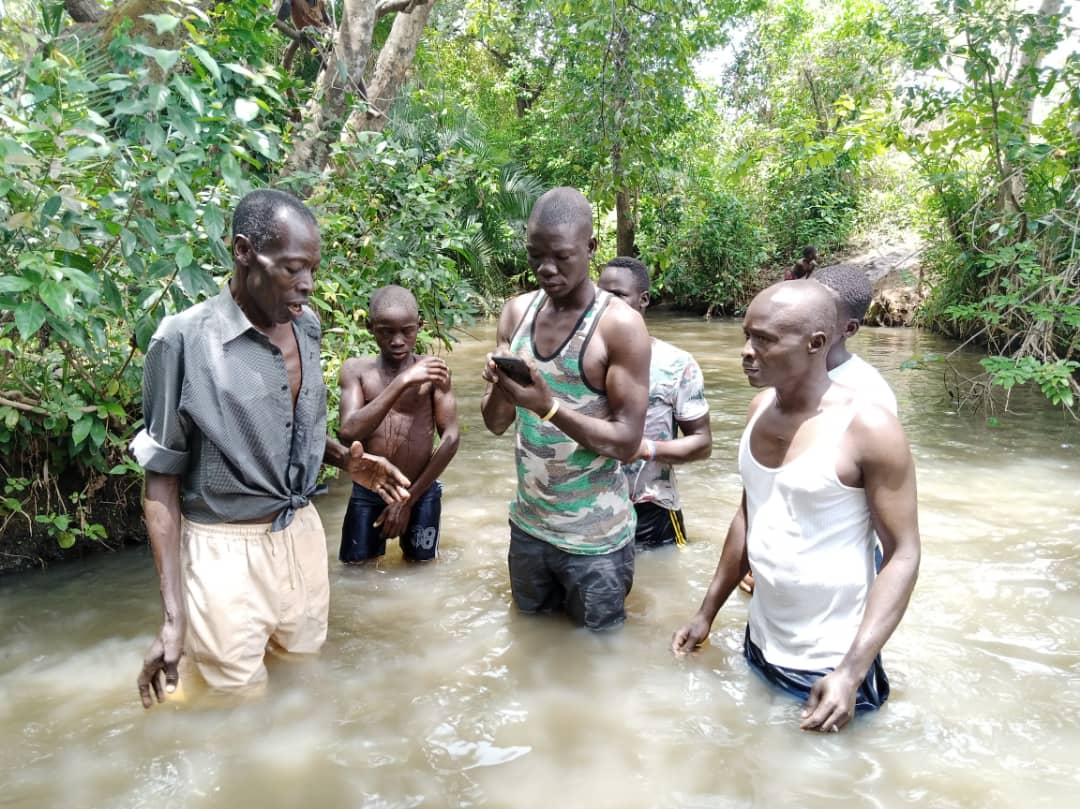 A group of men are kneeling in a river looking at their phones.