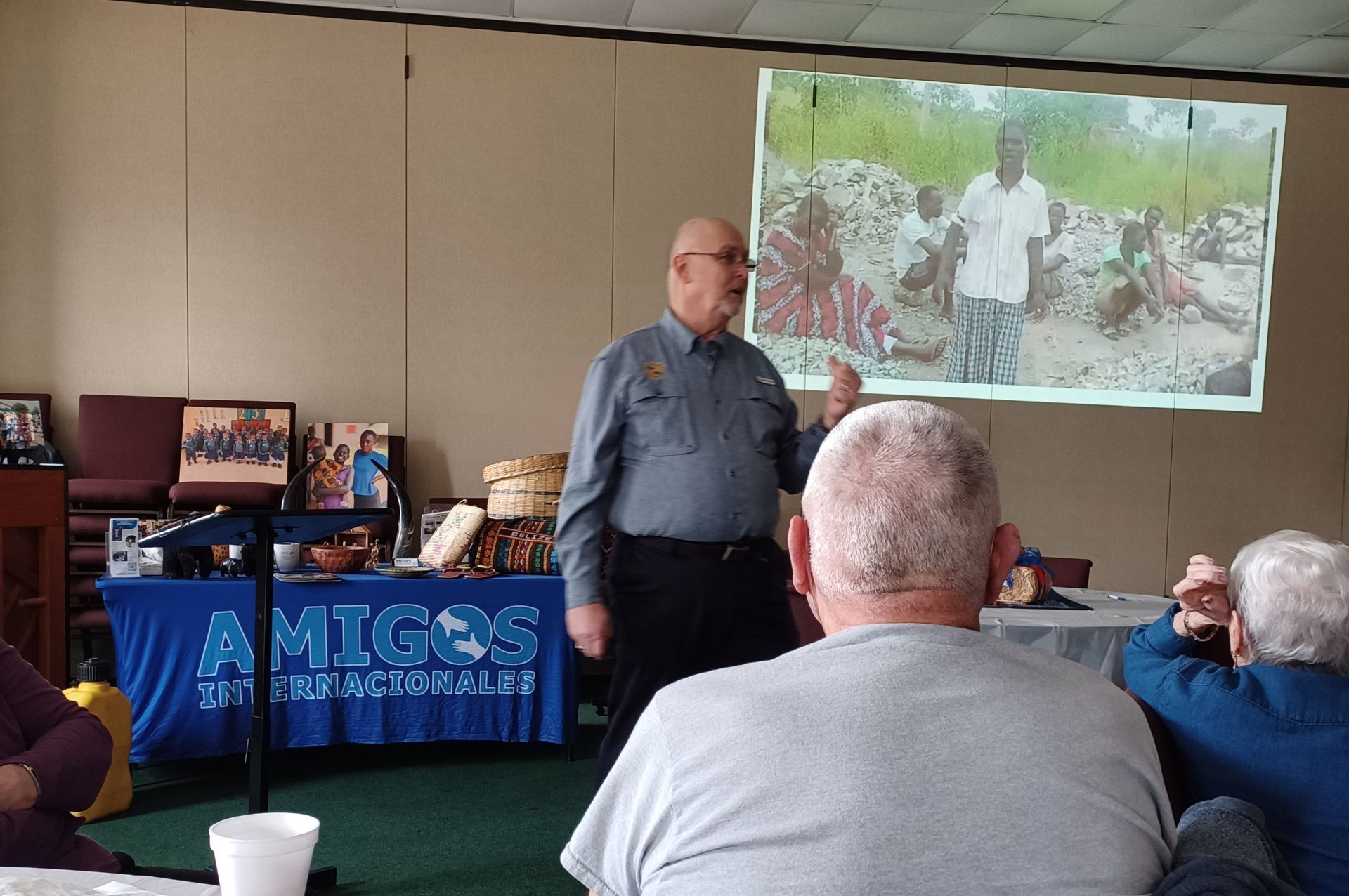 A man is giving a presentation in front of a screen that says amigos